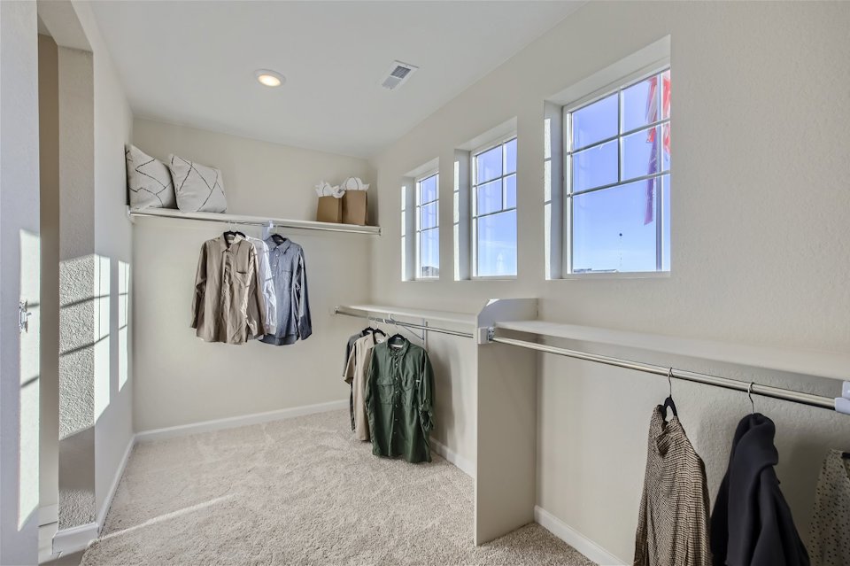 A room with a window and clothes on the wall.