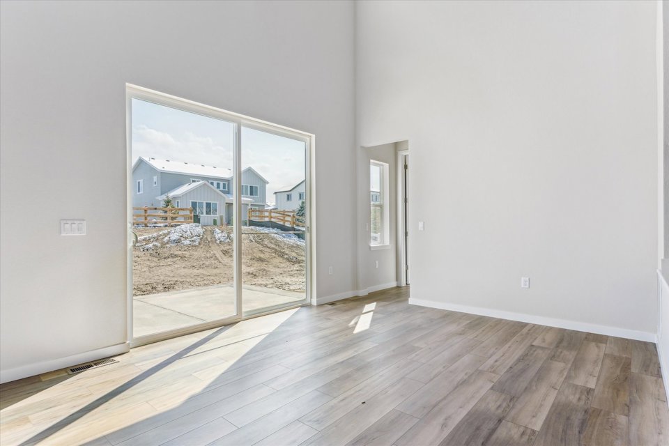 A room with a wood floor and a window with a view of a beach and a building.