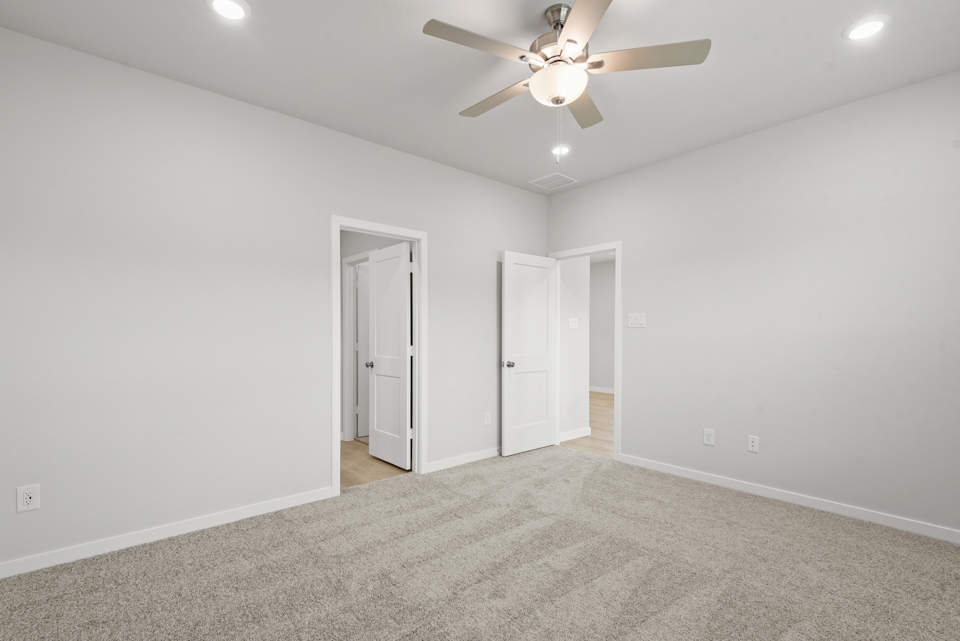 A room with a ceiling fan and white walls.