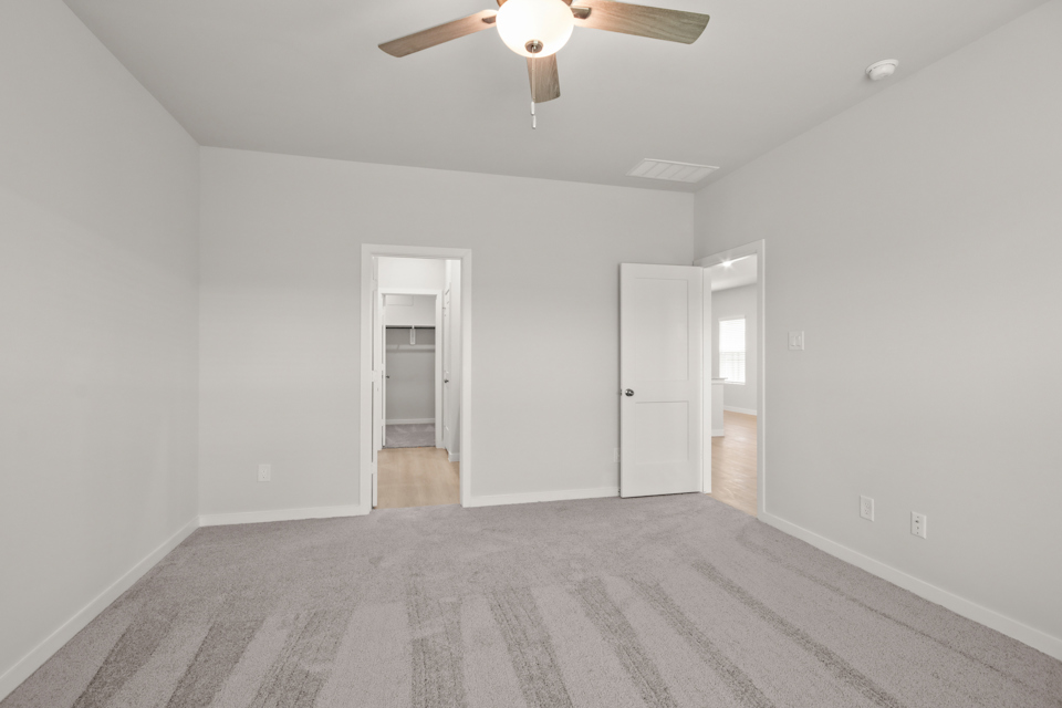 A room with a ceiling fan and a carpet.