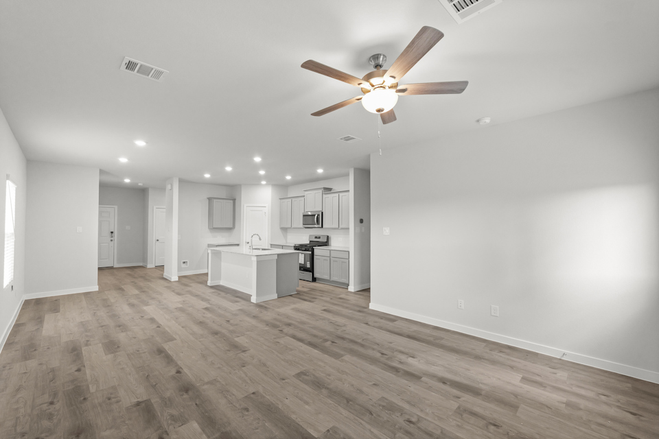 A large empty room with a ceiling fan and a wood floor.