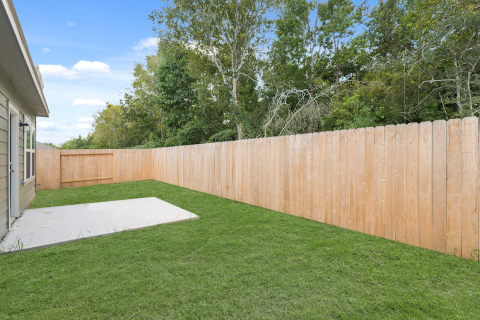 A fenced in yard with a wood fence and trees in the background.