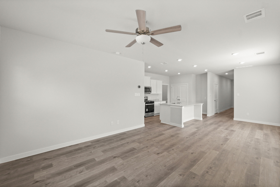 A large empty room with a ceiling fan and a wood floor.