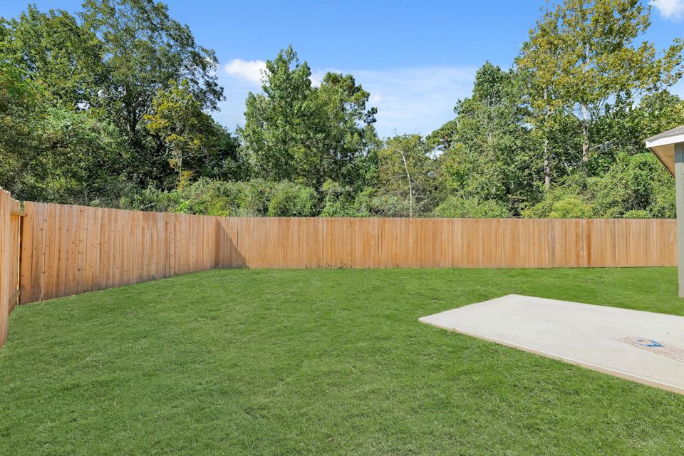 A fenced in yard with a wood fence and trees in the background.