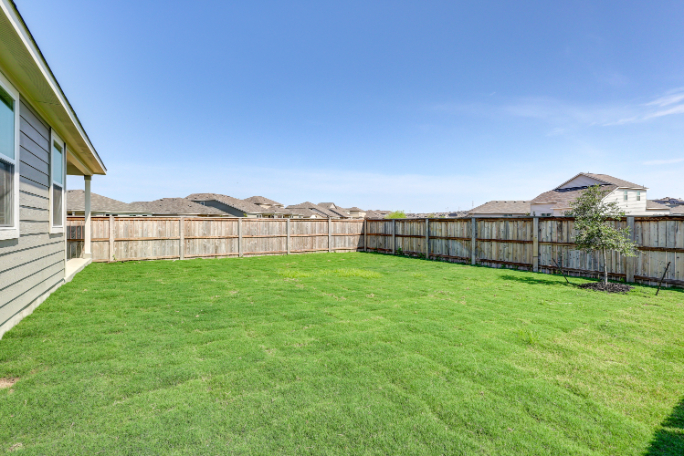 A fenced in yard with a house and trees in the background.